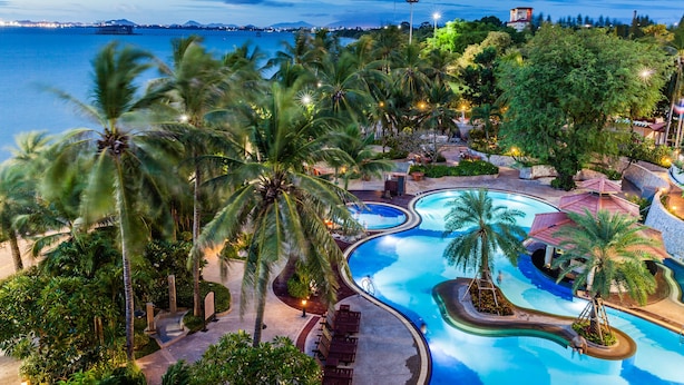 Un área de piscina en un resort, con palmeras, un diseño de piscina sinuoso y vistas al mar.