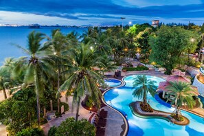 Un área de piscina en un resort, con palmeras, un diseño de piscina sinuoso y vistas al mar.