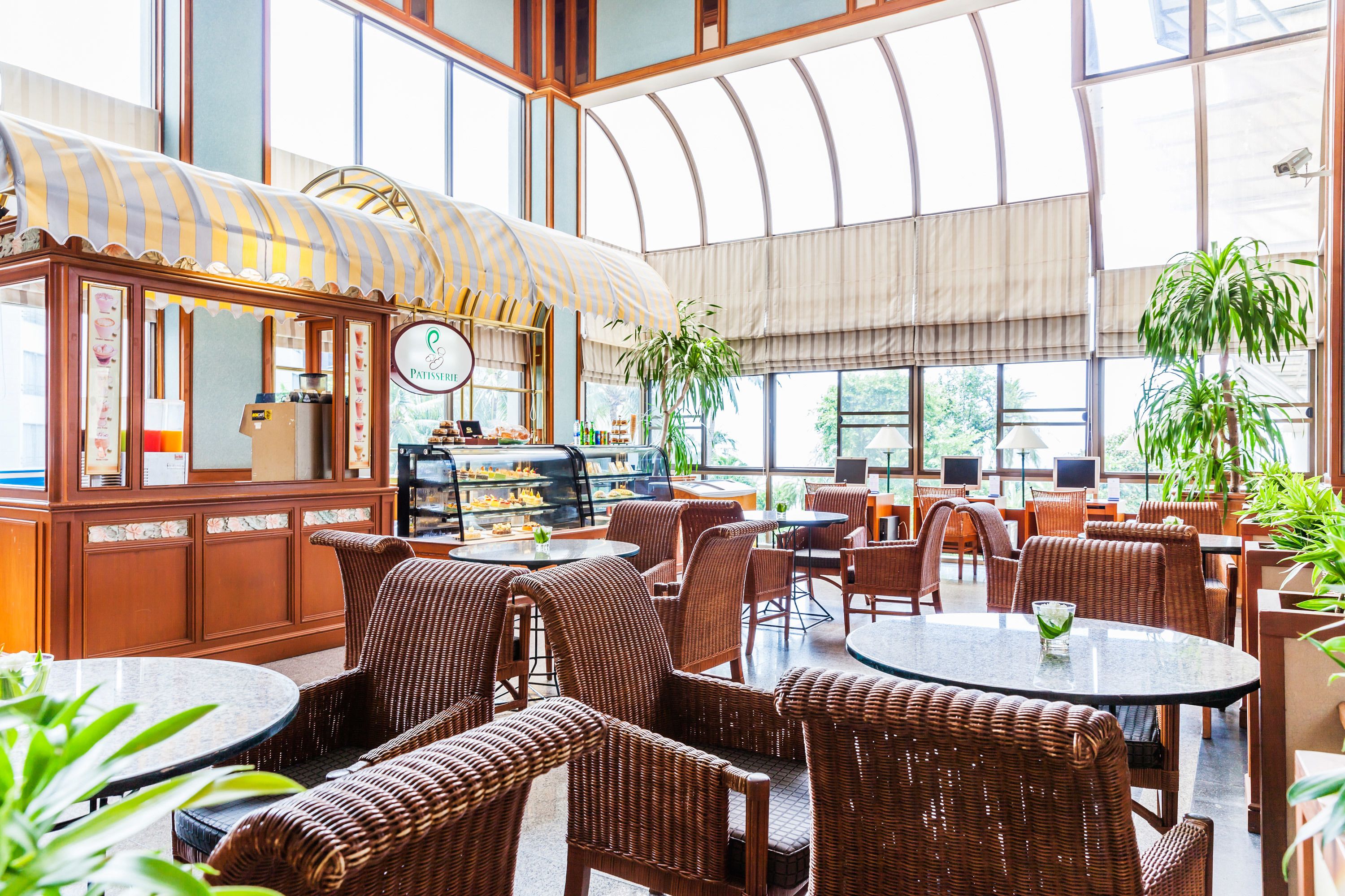 A spacious cafe with wicker furniture, a coffee station, and large windows offering natural light.