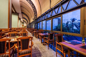 A restaurant with wooden tables and chairs, large windows, and a curved ceiling structure. - Cholchan Pattaya Beach Resort (Pattaya)