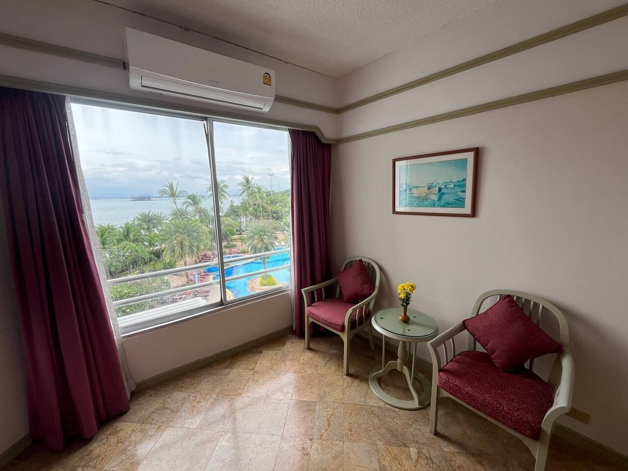 A room with a large window, two chairs, a small table, and a painting on the wall.