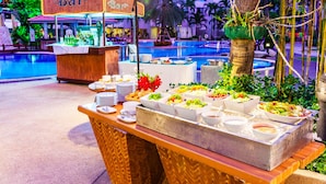 Zona de bufé con un letrero que dice 'Bar', diferentes platos de comida y una piscina al fondo.
