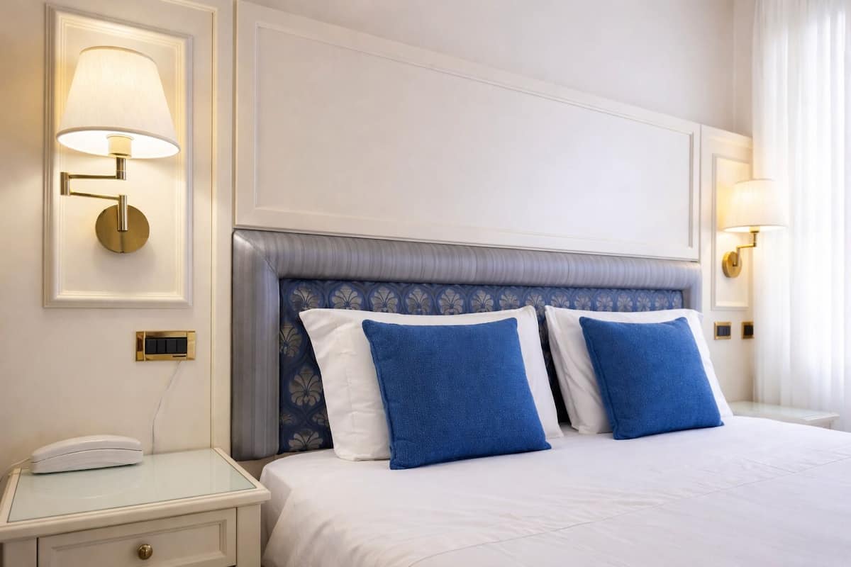 A hotel room with a large bed, two bedside lamps, a bedside telephone, and a nightstand with a lamp.