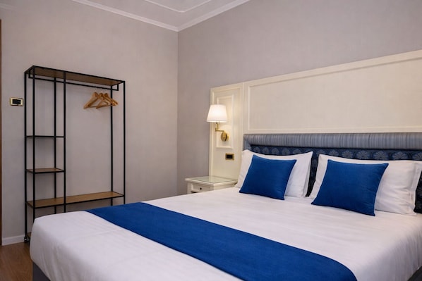 A hotel room with a large bed, a wardrobe with hanging space, a bedside table with a lamp, and a nightstand.