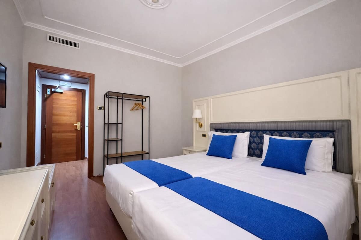 A hotel room with a large bed, a wardrobe, a desk, and a nightstand with a lamp.