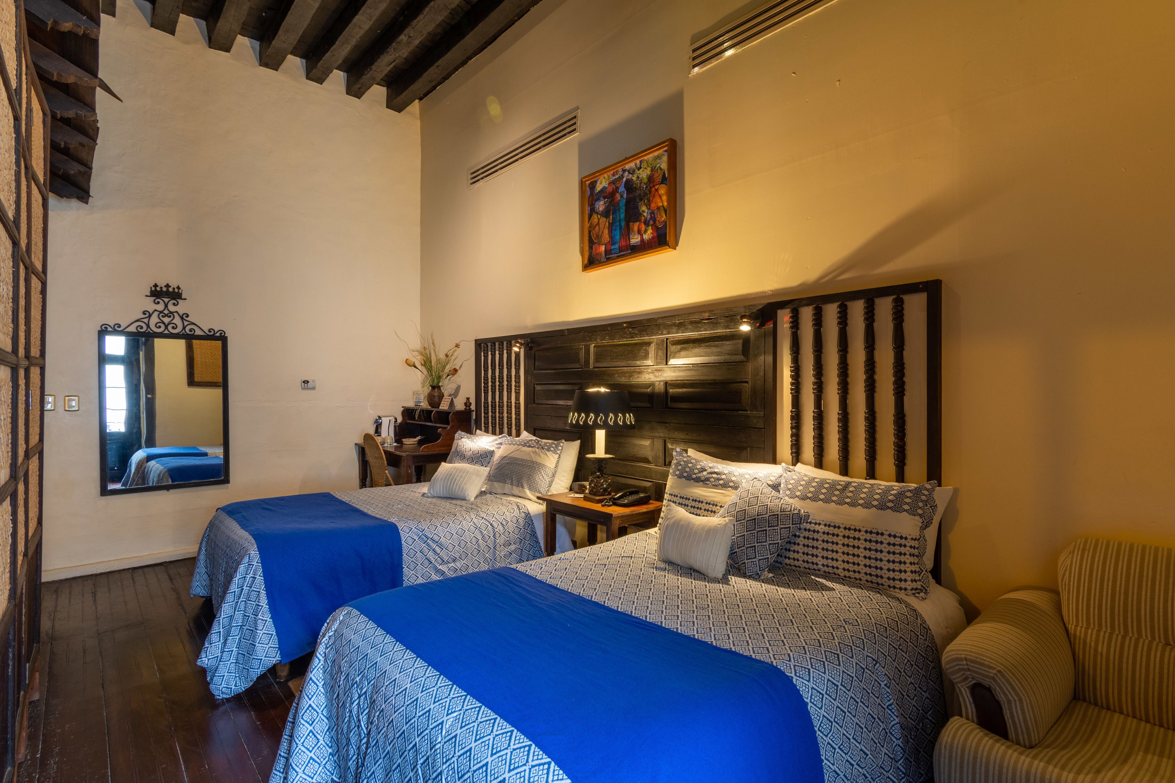 Habitación de hotel con dos camas, un espejo grande, un cuadro en la pared y techo de madera.