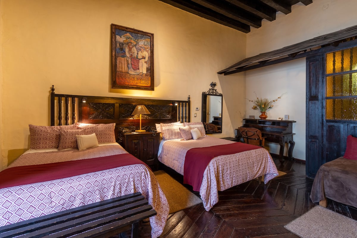 Une chambre traditionnelle avec deux lits, des meubles en bois, un tableau au mur et une fenêtre avec des vitres décorées.