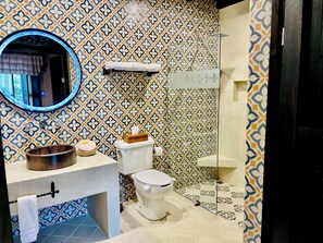 A bathroom with a patterned tile backsplash, a round mirror, a sink with a wooden bowl, a toilet, and a shower area. - Hotel Mansion Iturbe (Patzcuaro)