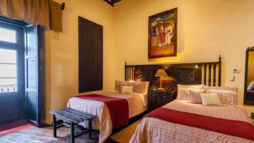 Habitación de hotel con dos camas, un banco, una puerta de madera y un cuadro en la pared.