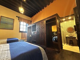 Habitación de hotel con cama, escritorio, armario, baño con lavabo y espejo, y un cuadro en la pared.