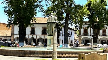 Une place publique avec une fontaine, entourée de bâtiments historiques dotés d’arcs en plein cintre et d’un toit recouvert de tuiles.