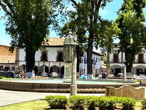 A public square with a fountain, surrounded by historic buildings with arched windows and a tiled roof. - Hotel Mansion Iturbe (Patzcuaro)