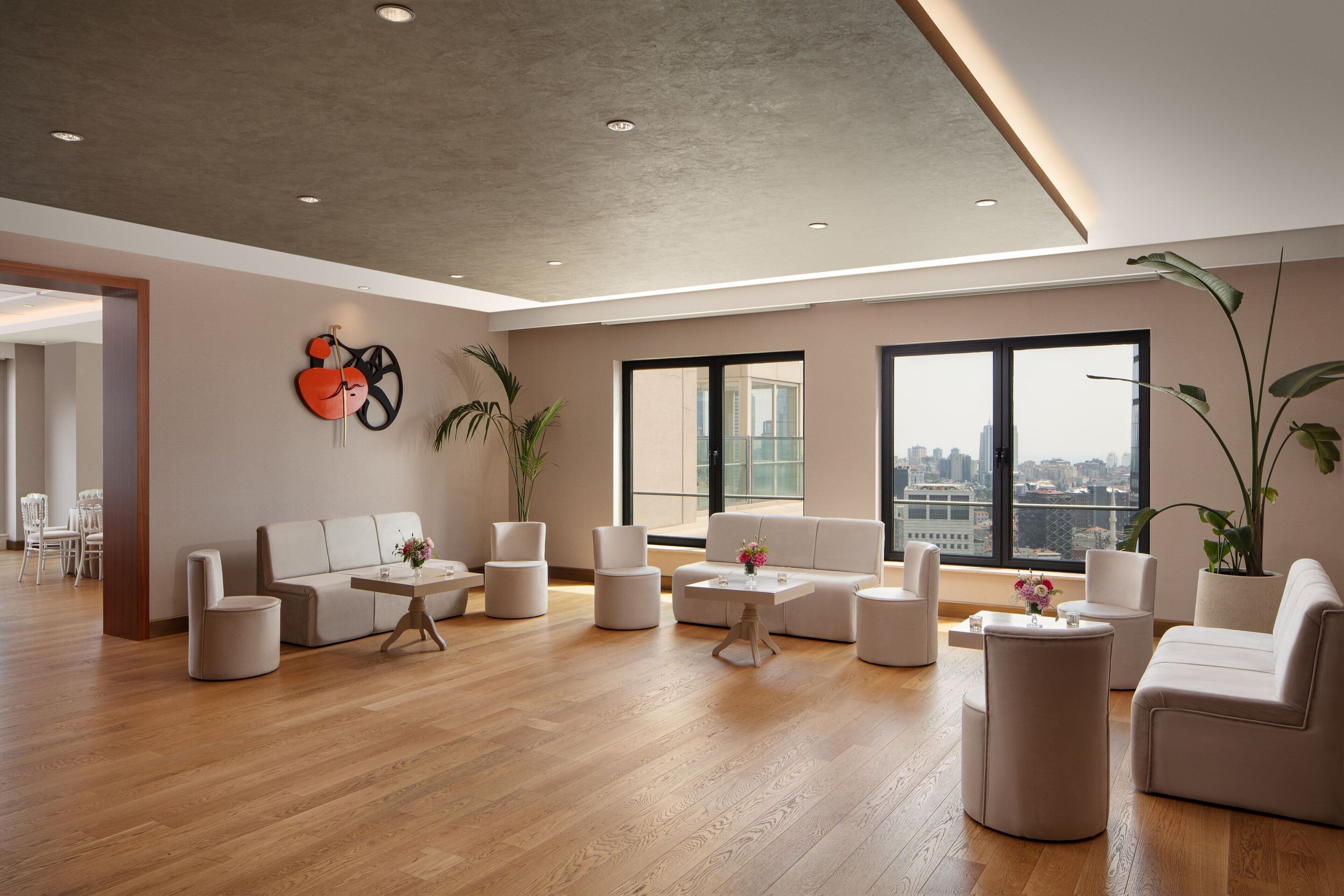 A spacious living room with a high ceiling, large windows, and a city view.
