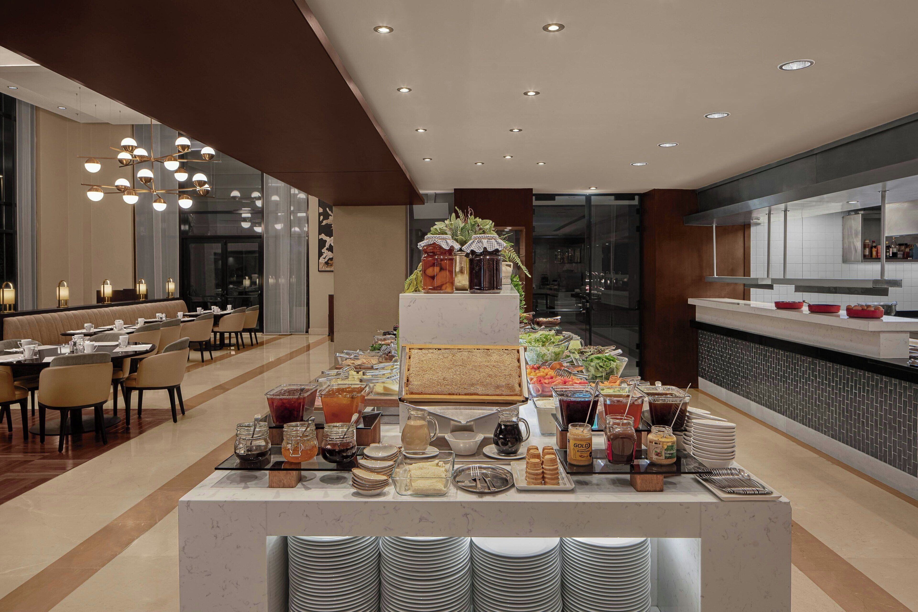 A buffet setup with various food items and beverages, a seating area with tables and chairs, and a modern kitchen visible in the background.