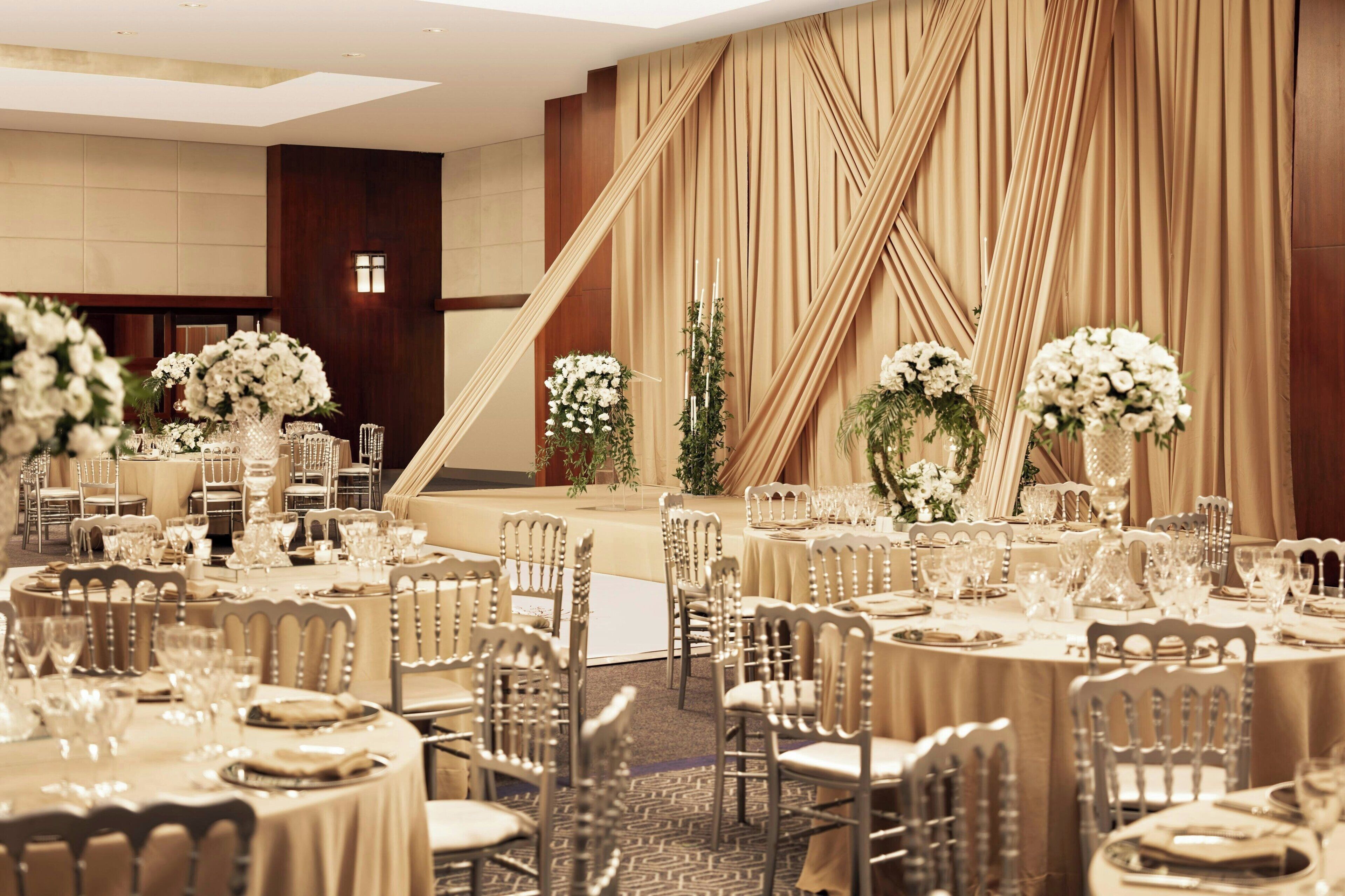 A banquet hall with round tables set for a formal event, featuring white floral centerpieces and elegant table settings.