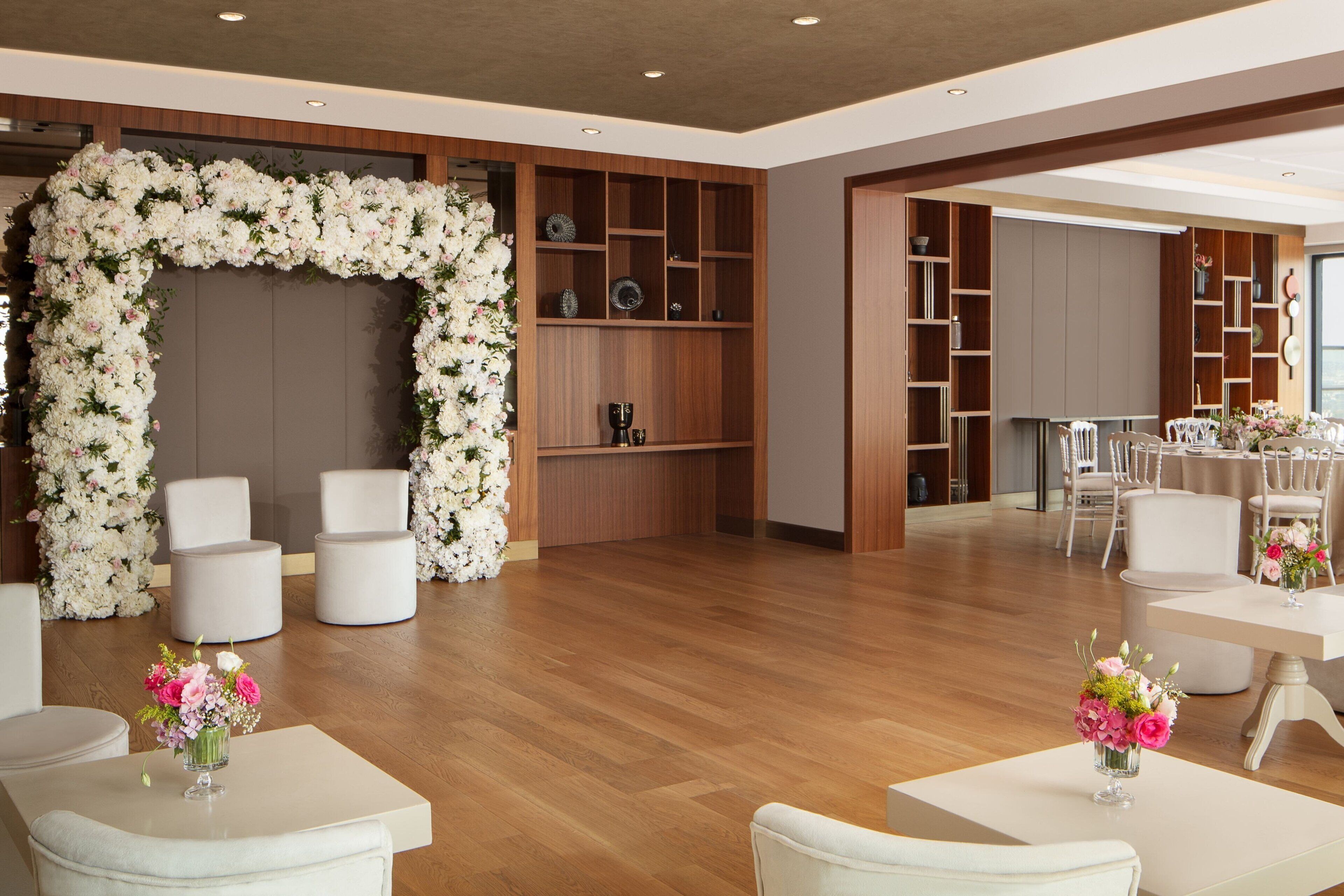 A spacious room with a floral arch, wooden shelving, and white furniture.