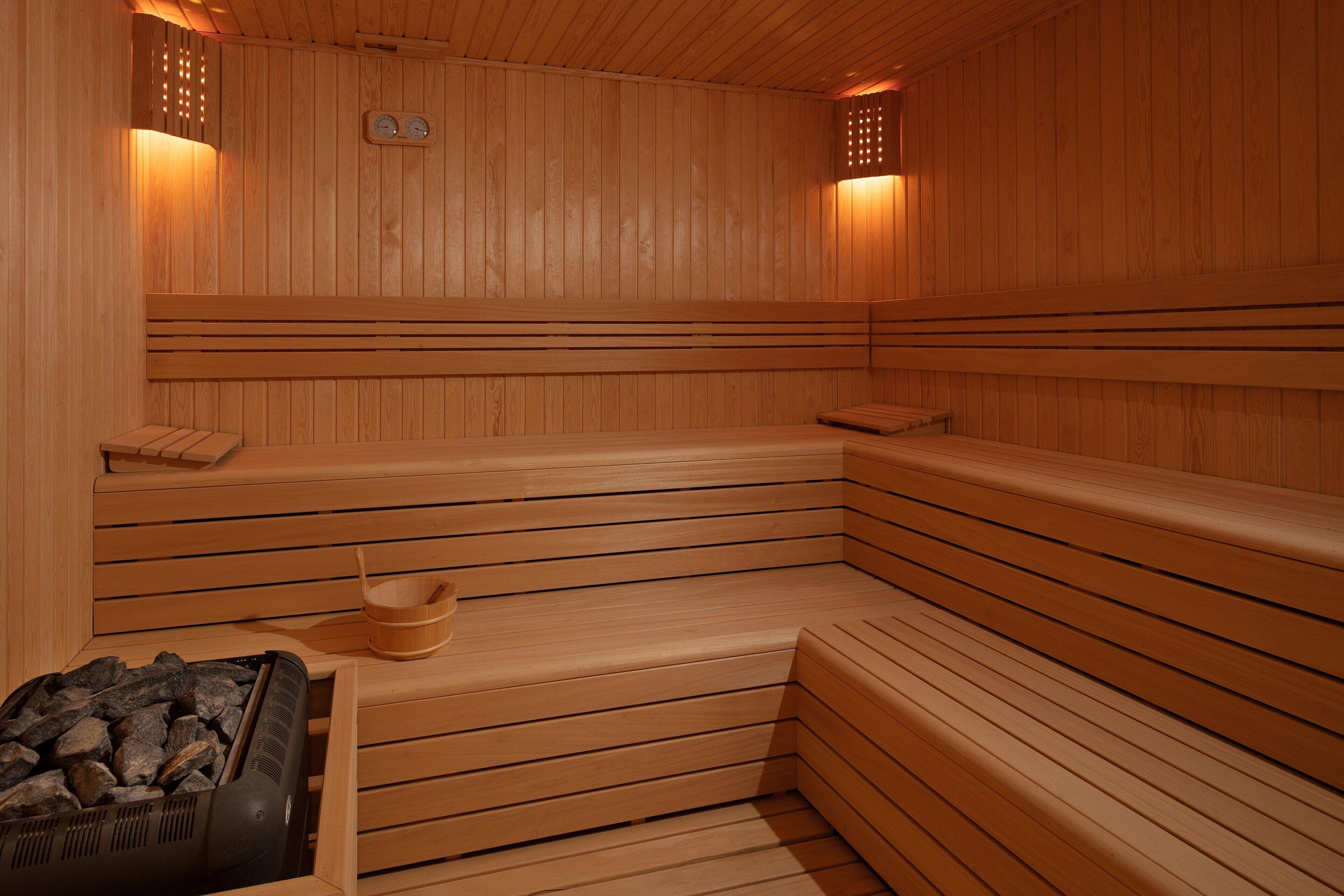 A sauna with wooden benches, a bench heater, and a wooden bucket.