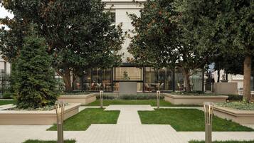A courtyard with a central pathway, surrounded by trees and a building with glass windows.