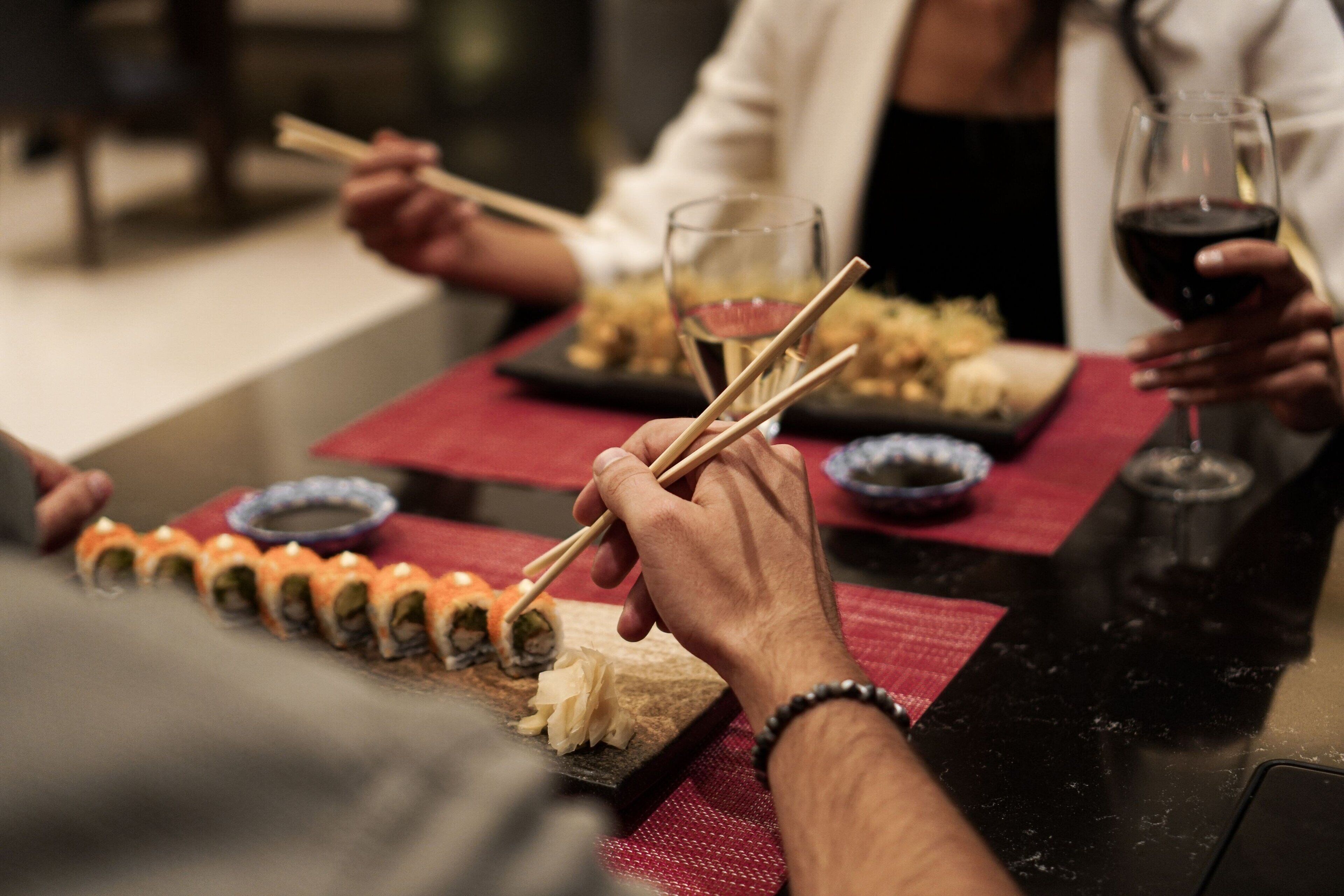 A dining table with sushi and wine glasses.