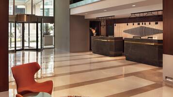 A modern lobby with a reception desk, a seating area with a round table, and a large glass door leading outside.