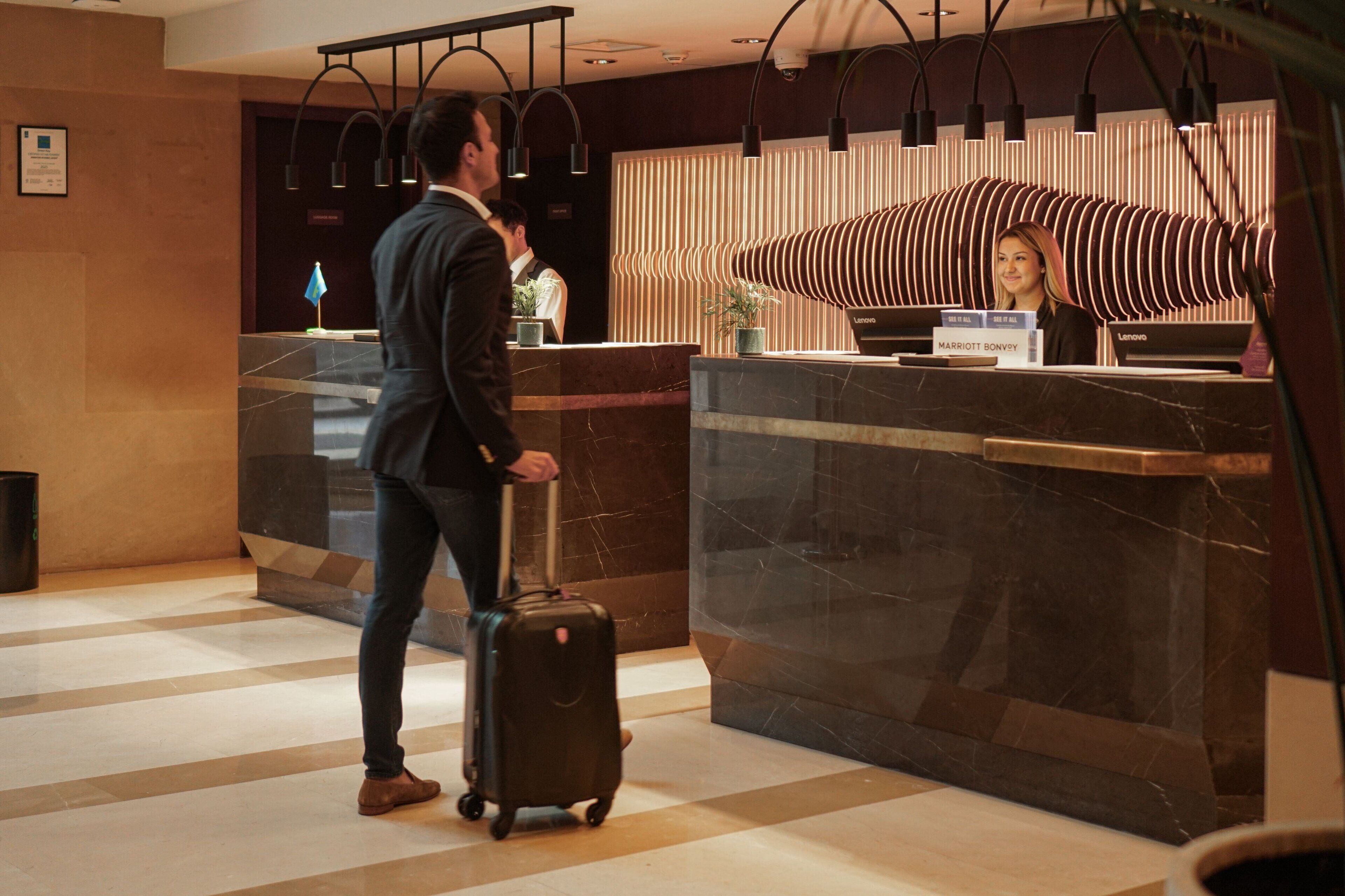 A hotel reception area with a marble counter, a receptionist, and a guest with a suitcase.