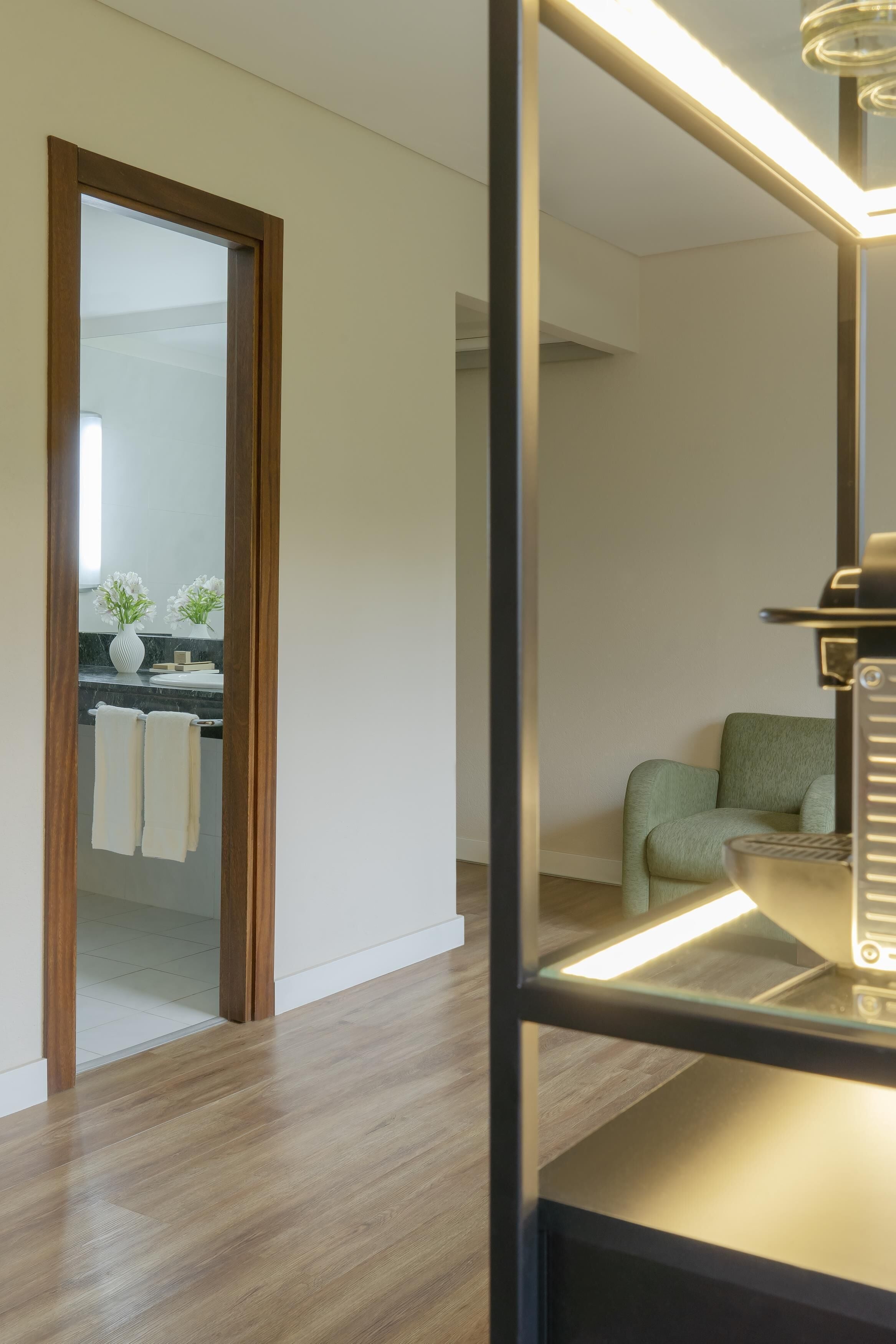 A modern bathroom with a wooden floor, a mirror, a green chair, and a towel rack.