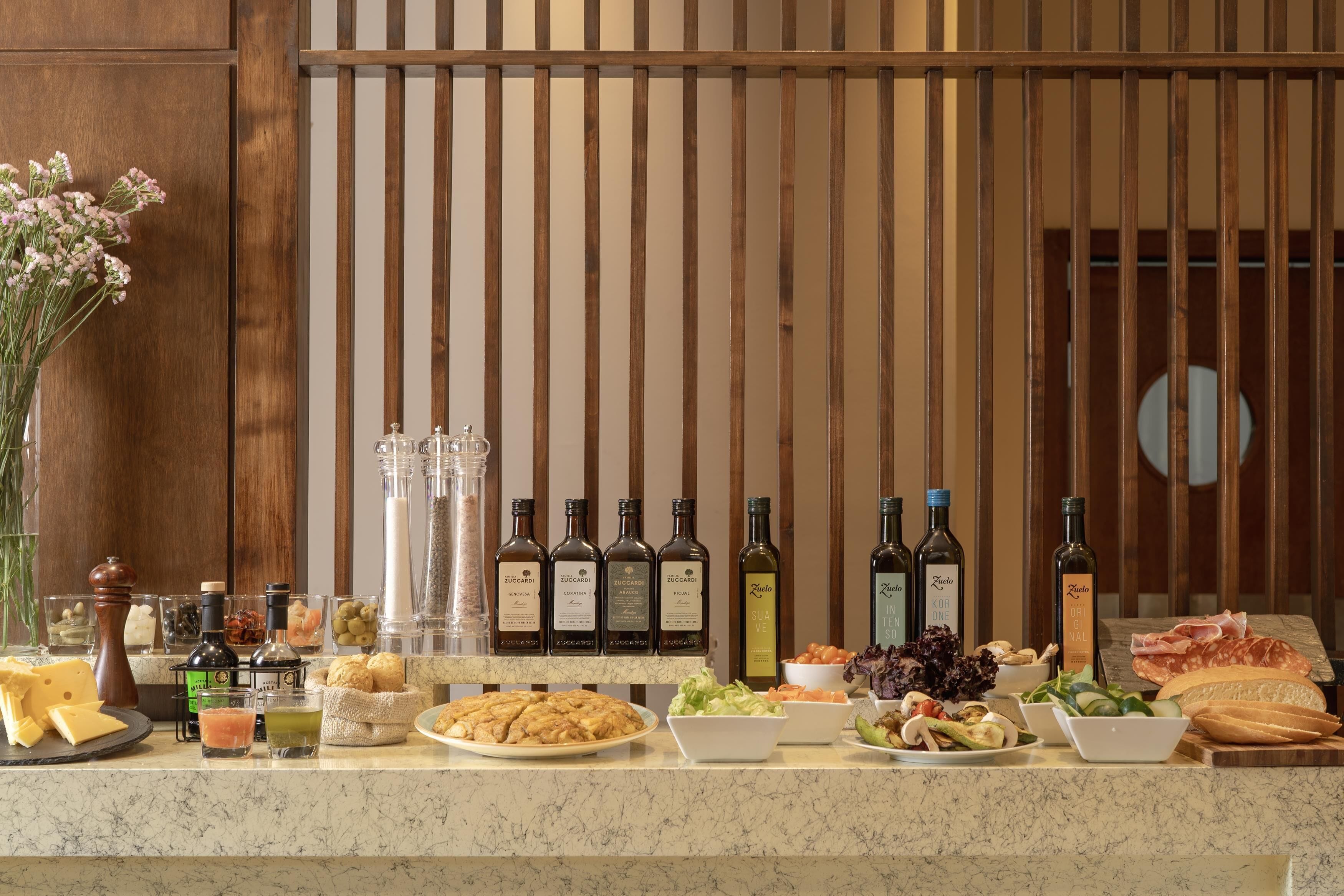 A buffet table with various food items, including cheese, bread, and salads, and several bottles of wine.