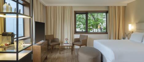 Habitación de hotel con una cama grande, dos sillones, una mesita, televisor y ventana con cortinas.