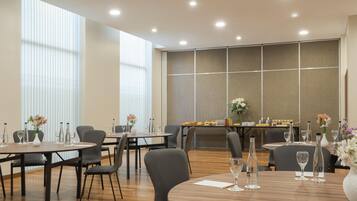 A modern dining area with round tables, grey chairs, and a long table with a buffet.