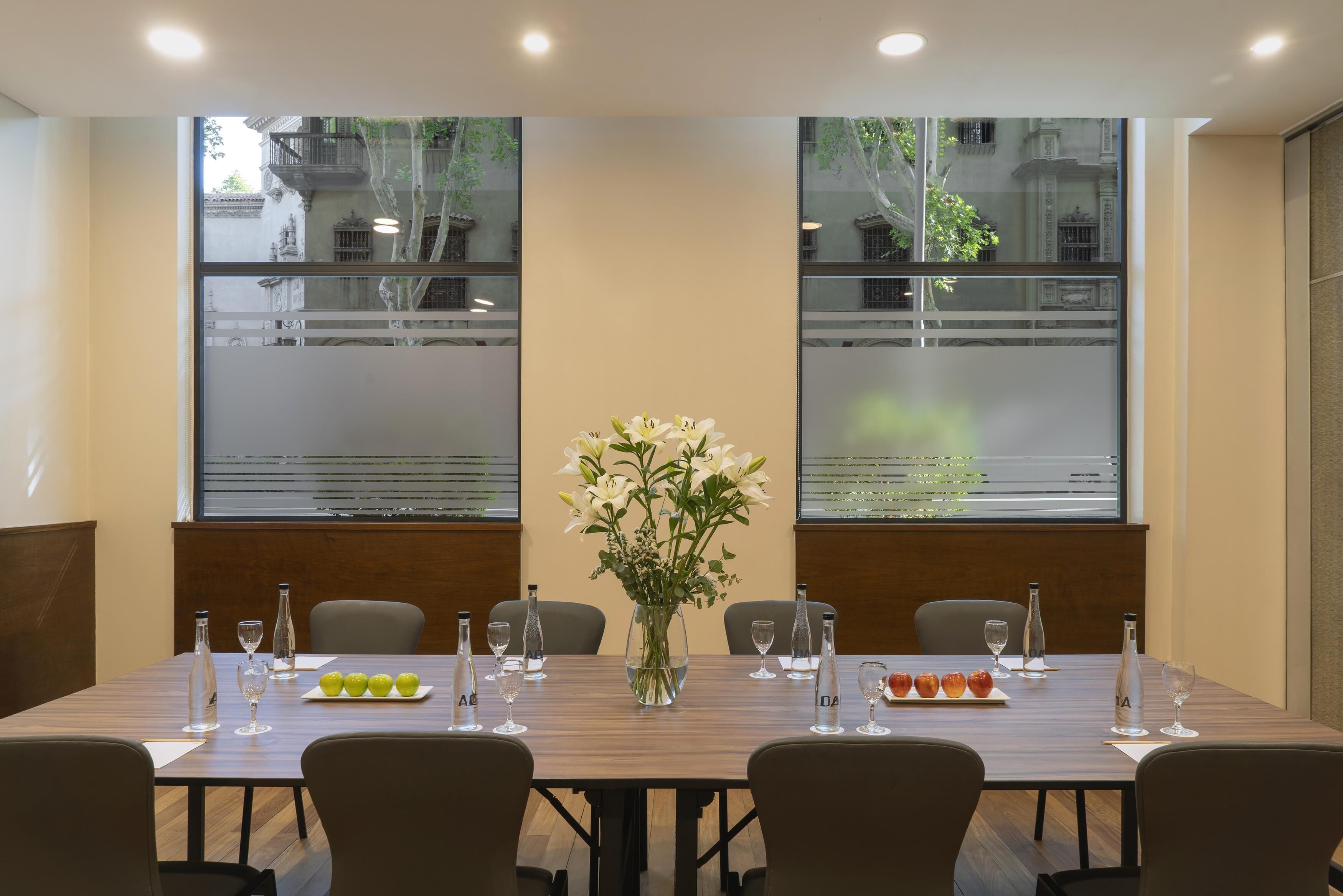 A conference room with a long table, chairs, a vase of flowers, and bottles of water and wine.