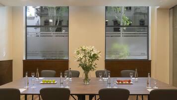 A conference room with a long table, chairs, a vase of flowers, and bottles of water and wine.