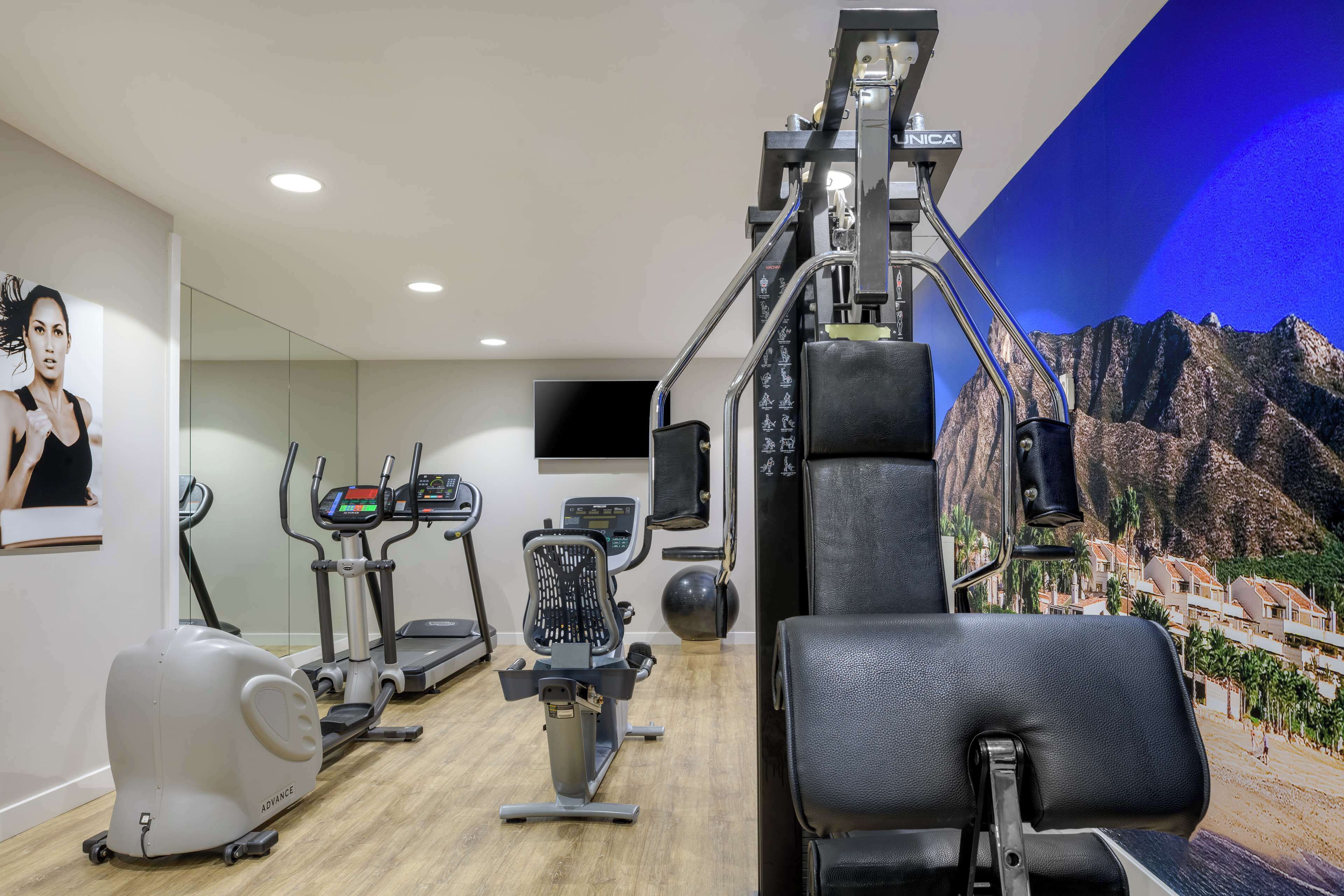 Un gimnasio con diversos equipos de ejercicio, un espejo grande y un televisor montado en la pared.