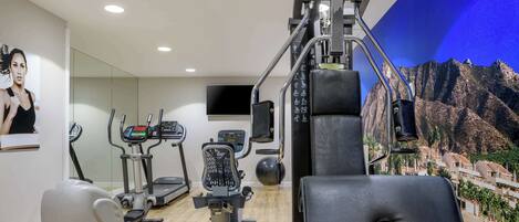 Un gimnasio con diversos equipos de ejercicio, un espejo grande y un televisor montado en la pared.
