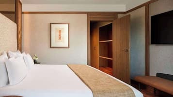 Une chambre d’hôtel avec un grand lit, une table de chevet avec des livres, un tableau encadré au mur, une armoire et un banc.