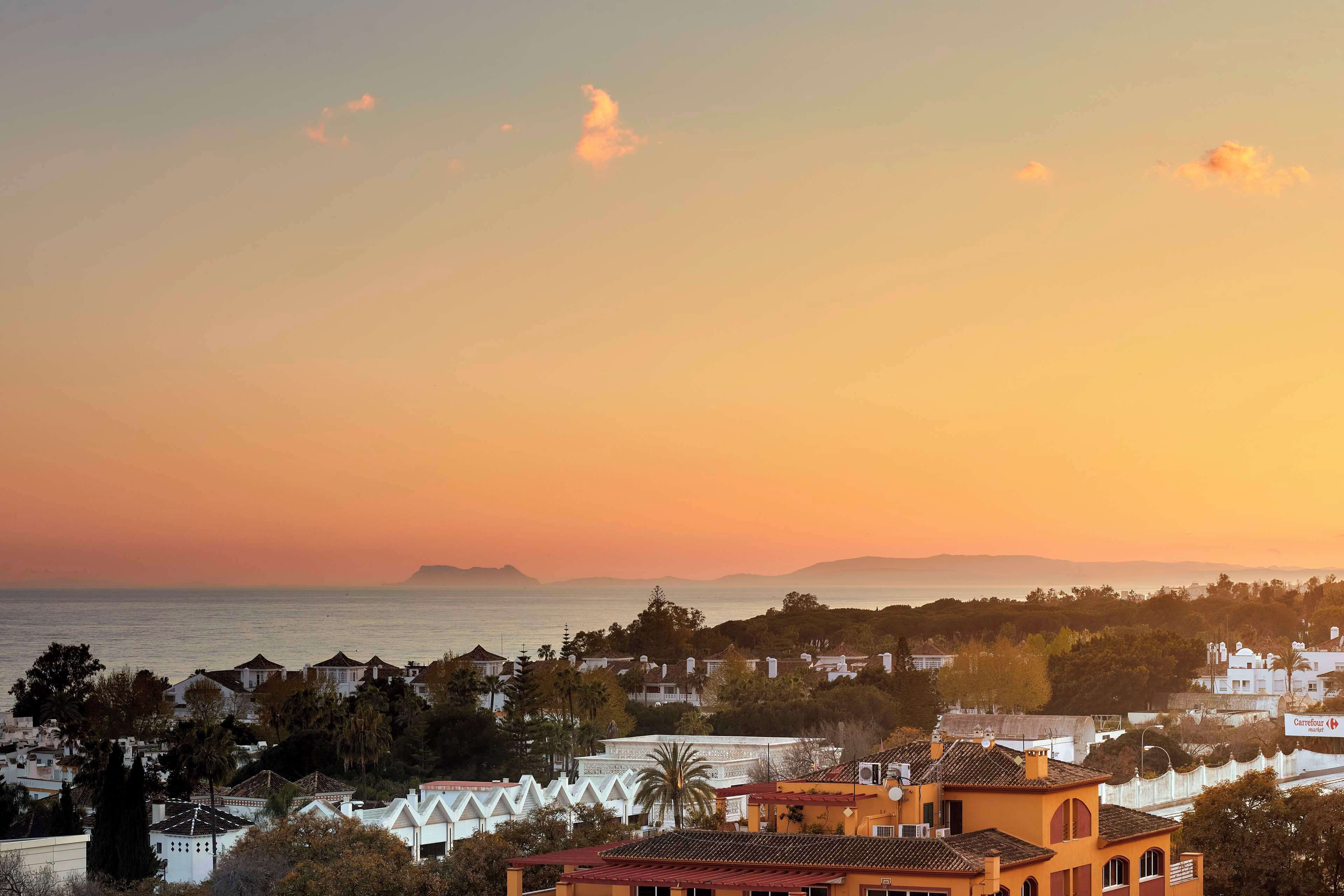 A coastal town at sunset with buildings and a view of the sea.