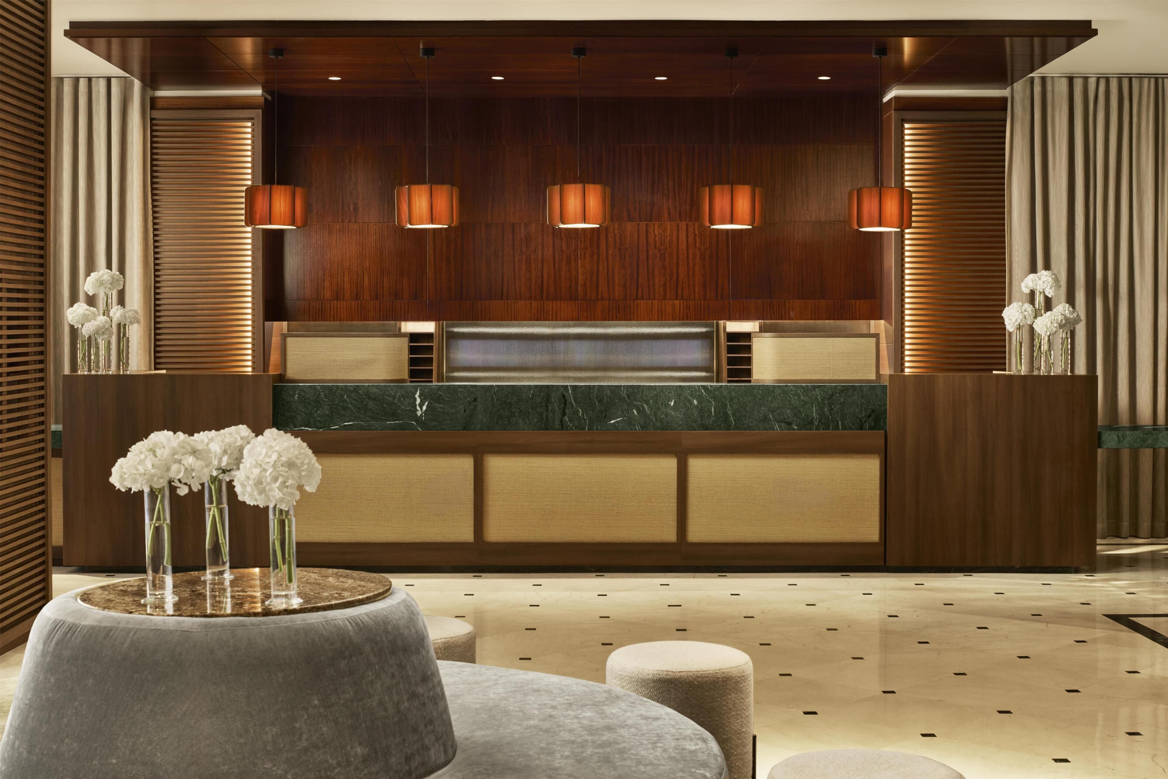 A reception area with a wooden panel wall, three pendant lights, a marble counter, and a round table with vases.