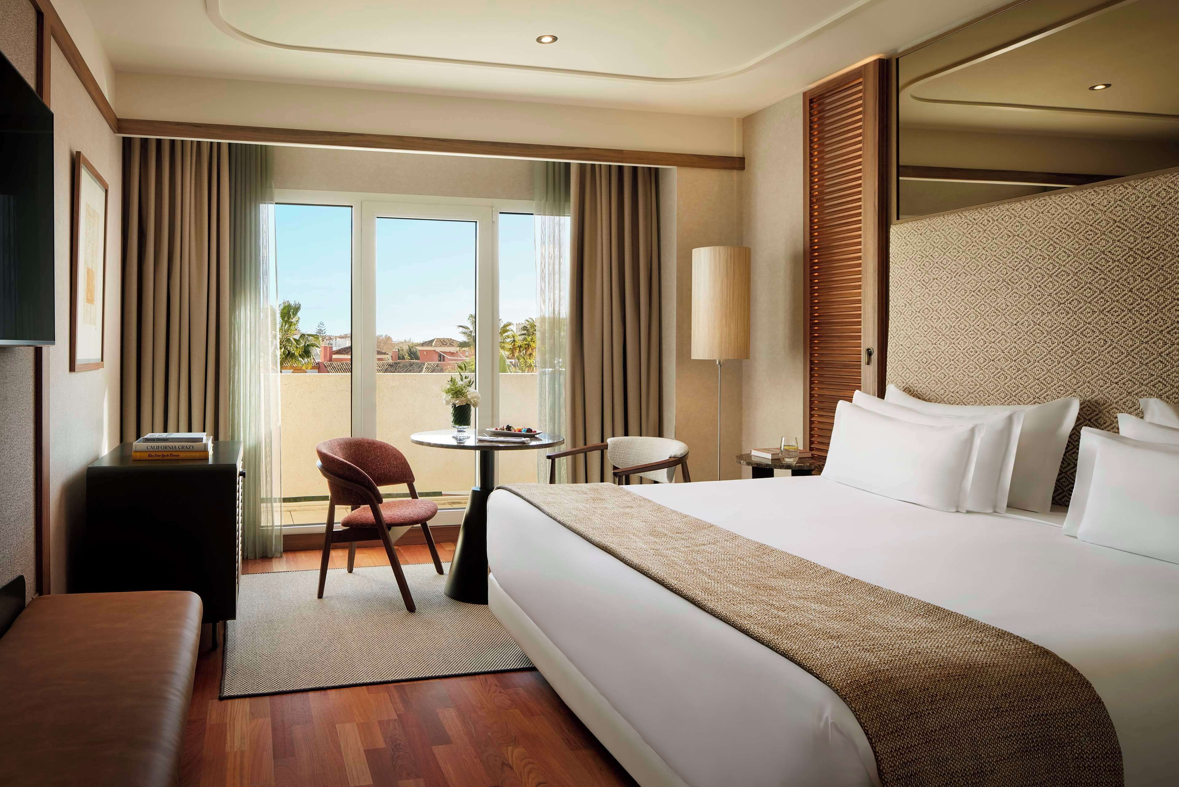 A hotel room with a large bed, a desk, a chair, and a view of the outdoors.