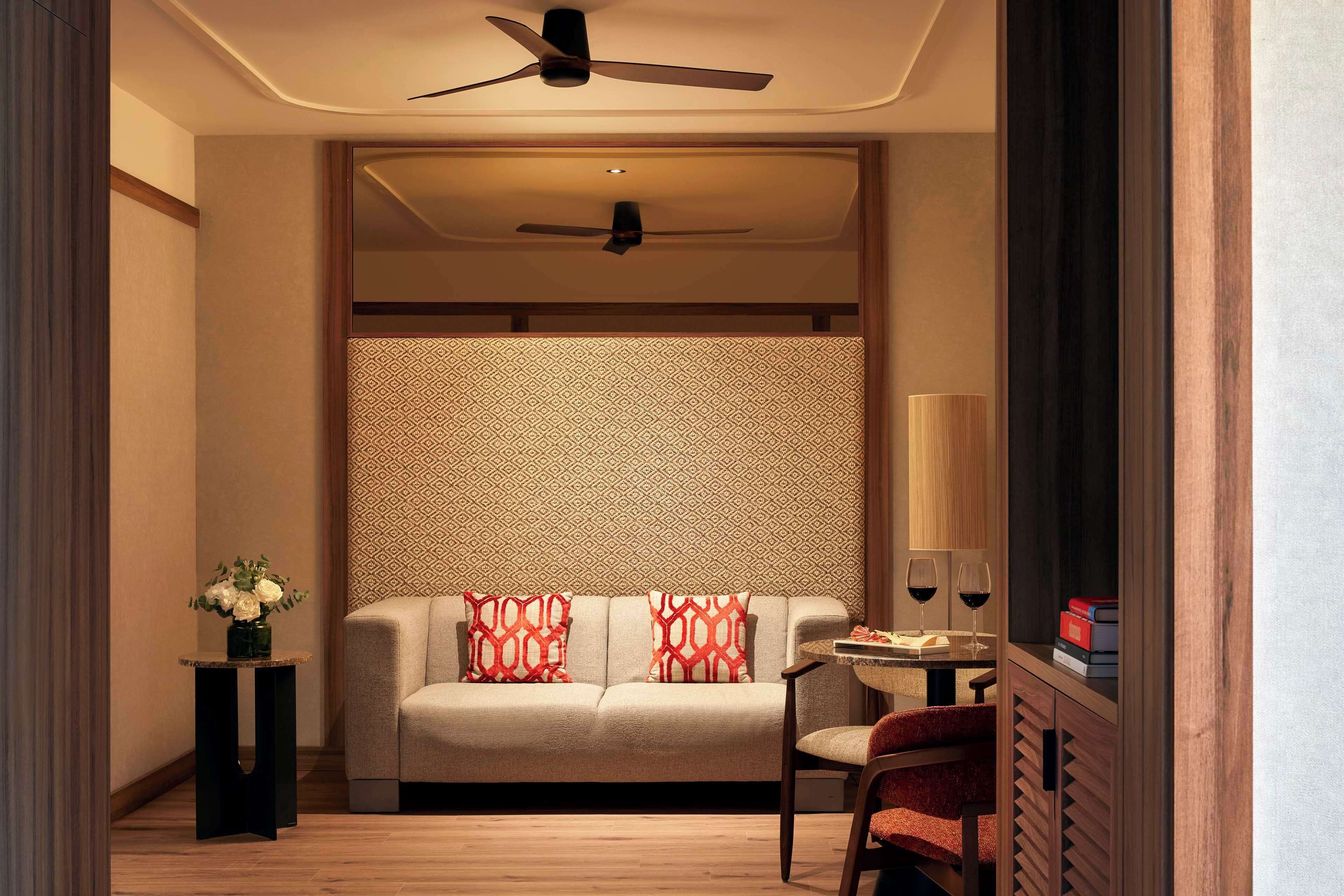 A modern hotel room with a sofa, a small table with a lamp, and a ceiling fan.