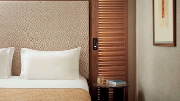 A hotel room with a bed, pillows, a small table with a book, and a wooden door with a patterned curtain.