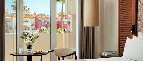 A hotel room with a bed, a table with a vase of flowers, a chair, and a view of the outside buildings.