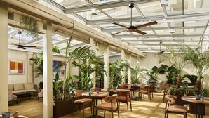 A spacious indoor area with tables and chairs, large windows, and ceiling fans.