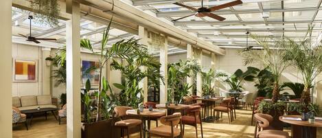 A spacious indoor area with tables and chairs, large windows, and ceiling fans.