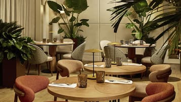 A dining area with round tables, chairs, and potted plants.