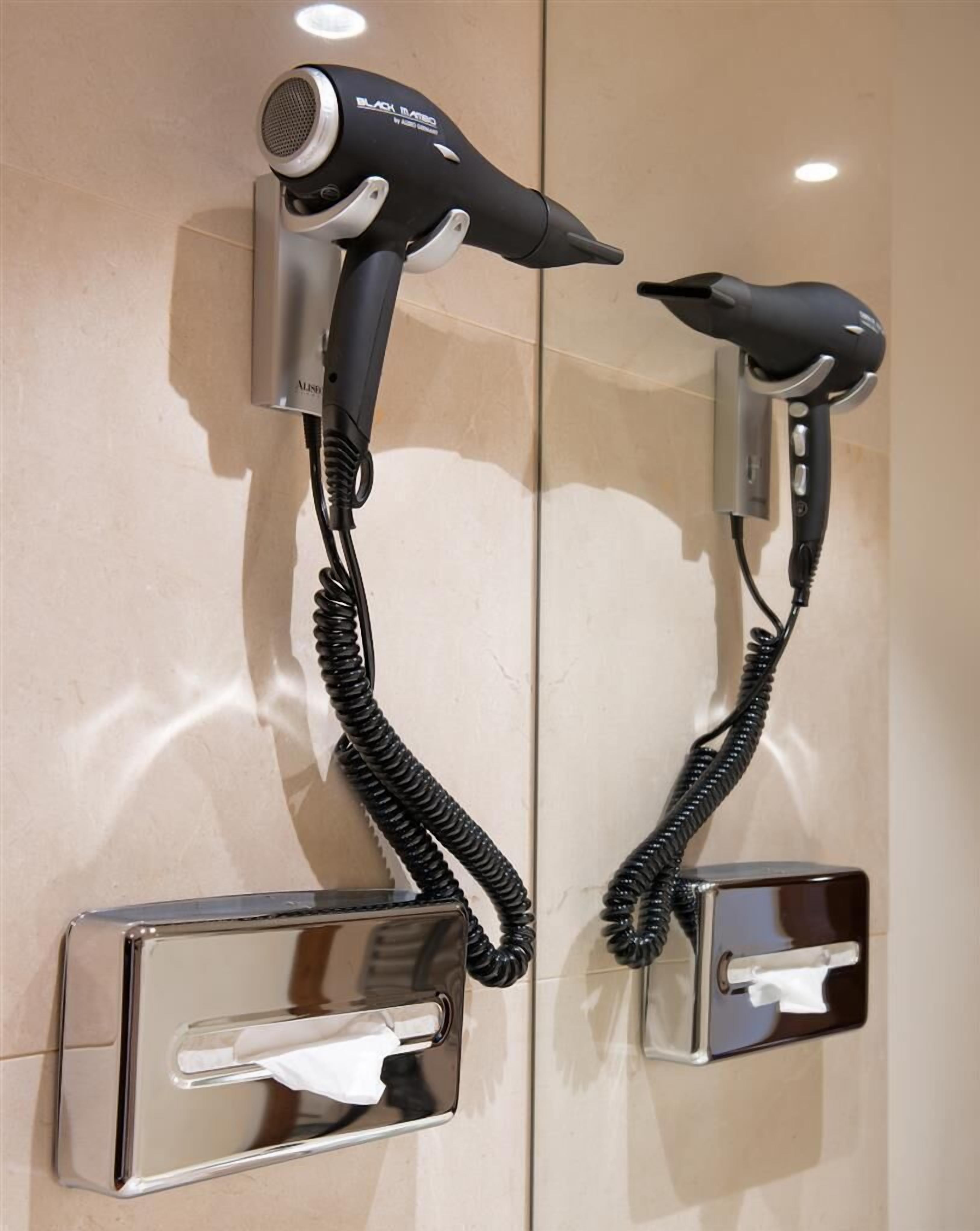 A wall-mounted hair dryer with a cord, a mirror, and a towel dispenser.