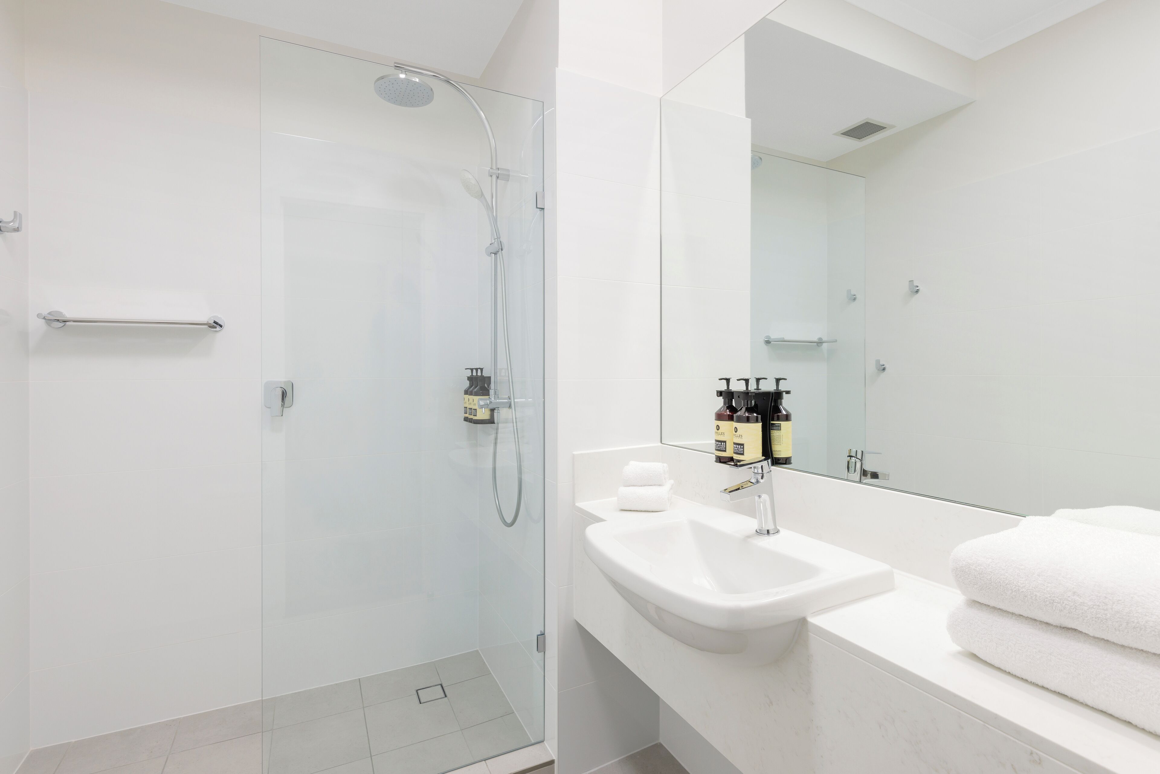A modern bathroom with a glass-enclosed shower, a white sink, and a large mirror.