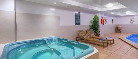 A spa area with a hot tub, lounge chairs, a small pool, and a wall-mounted information board.