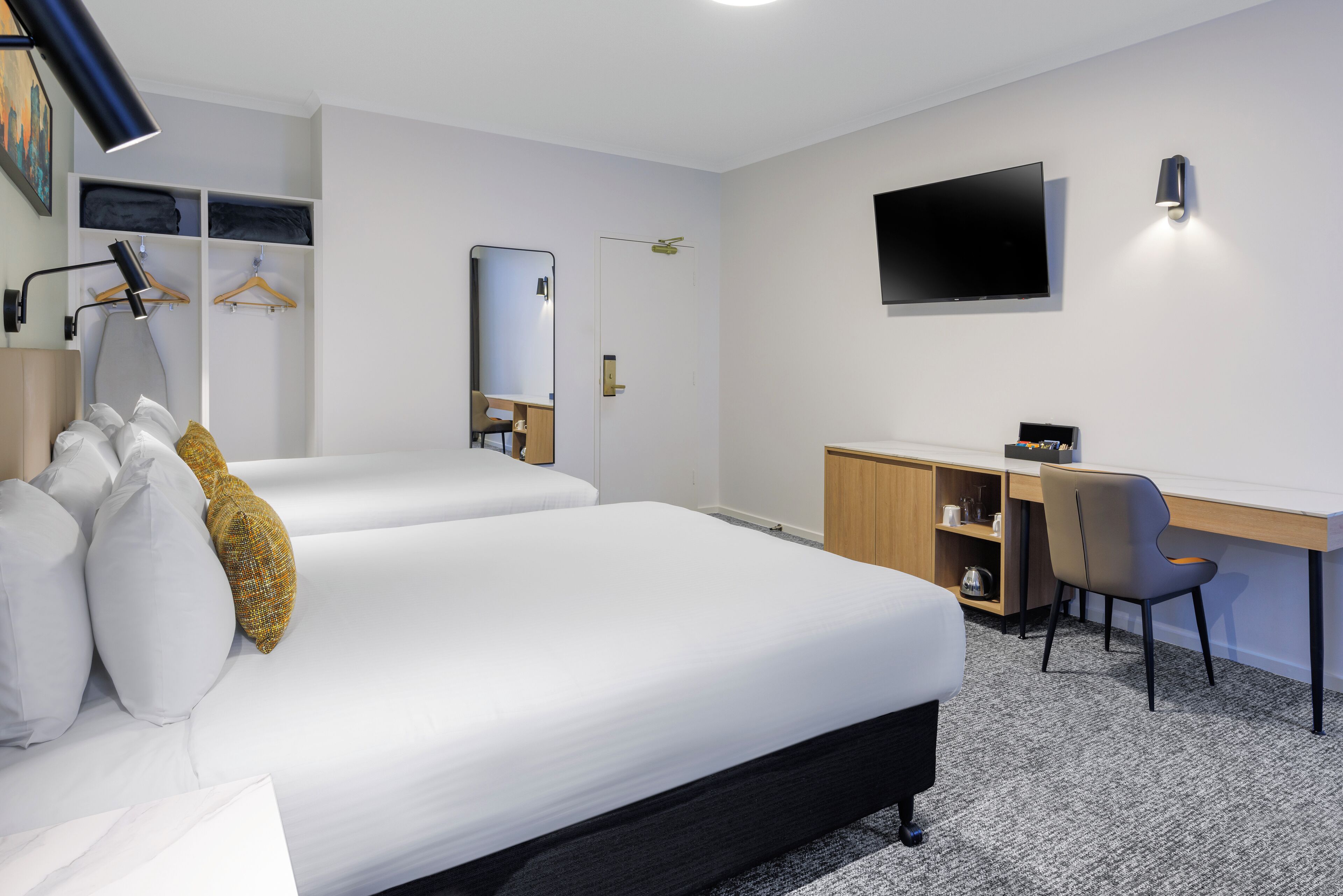 A hotel room with two beds, a desk, a chair, a TV, and a wardrobe.