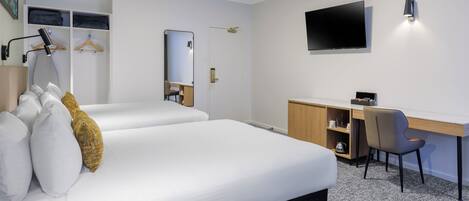 A hotel room with two beds, a desk, a chair, a TV, and a wardrobe.