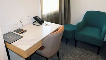 Hotellihuone, jossa on työpöytä, turkoosinsininen nojatuoli, puhelin ja esite työpöydällä.
