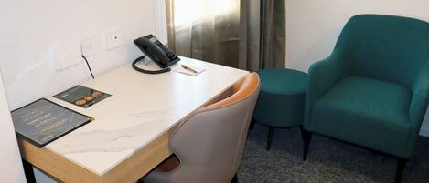 Une chambre d’hôtel équipée d’un bureau, d’un fauteuil turquoise, d’un téléphone et d’une brochure posée sur le bureau.